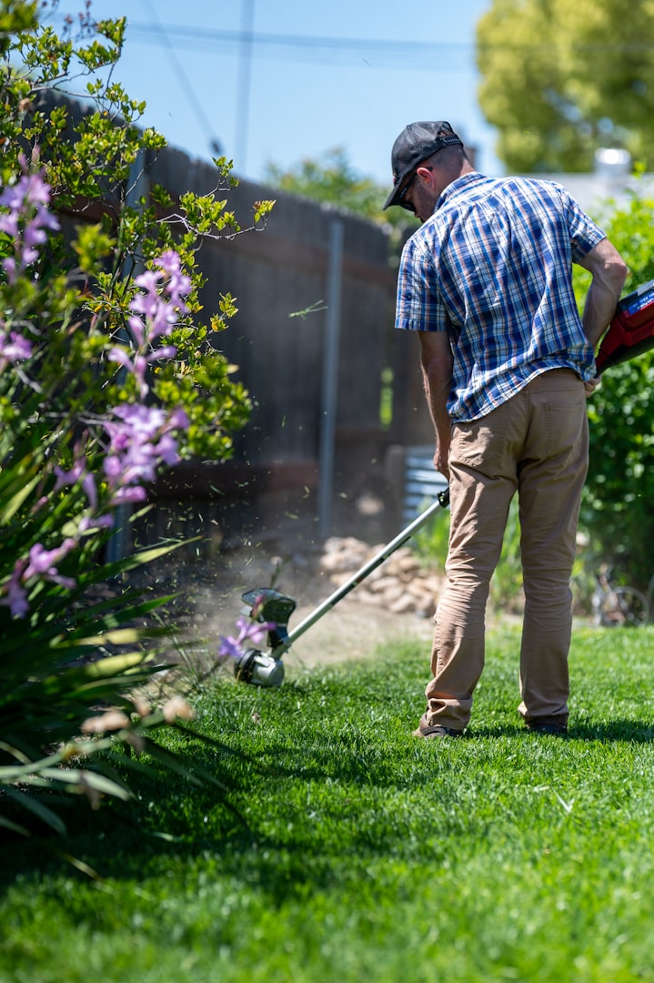 A person wearing a blue shirt and cap removes leaves from a roof gutter in a wooded area.